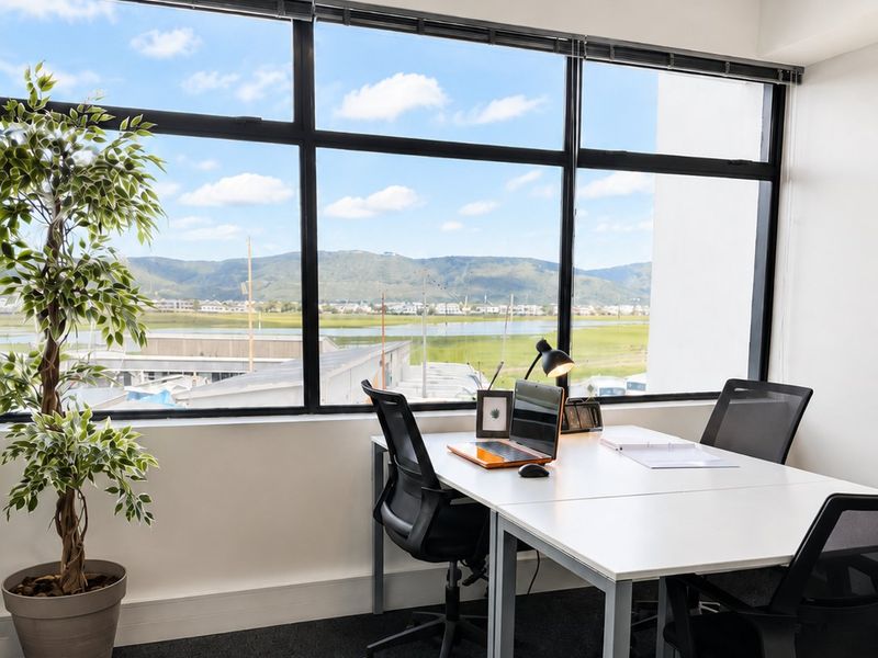 A bright office space featuring large windows with scenic landscape views and modern carpet flooring.