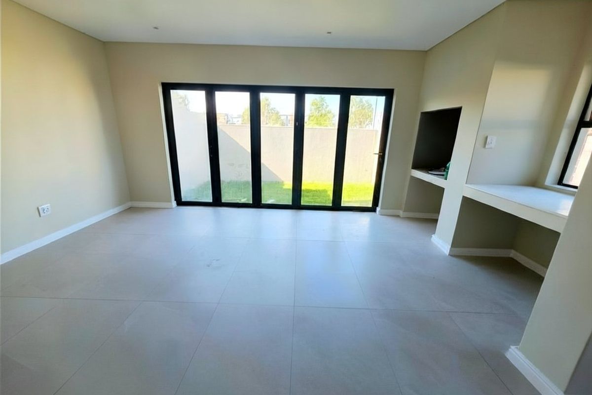 Spacious living area featuring large black-framed bi-fold doors opening to the garden and a convenient built-in braai area.