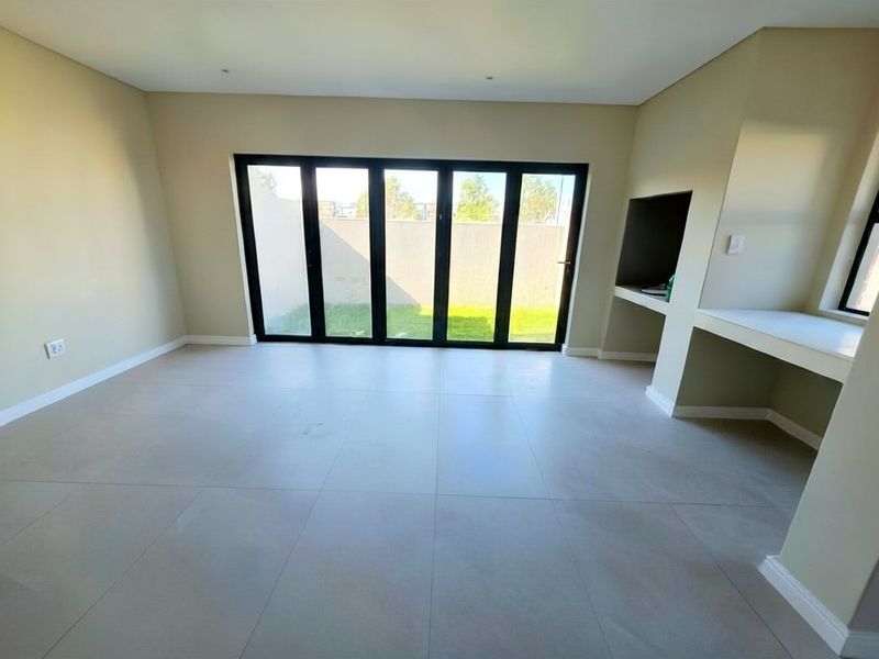 Spacious living area featuring large black-framed bi-fold doors opening to the garden and a convenient built-in braai area.