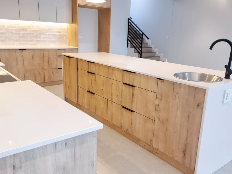 Modern kitchen featuring a large island with quartz countertops, light wood cabinetry, subway tile backsplash, and a sleek black gooseneck faucet.