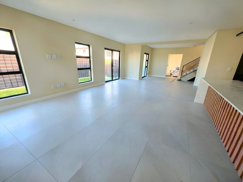 Spacious open-plan living area featuring large format floor tiles, modern staircase, and a kitchen island with contemporary slatted timber detailing.
