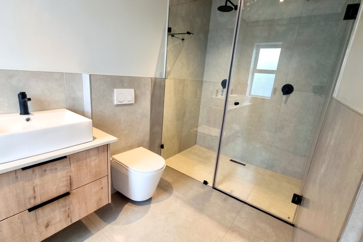 Modern bathroom featuring a wall-mounted vanity with vessel sink, wall-hung toilet, and a spacious walk-in shower with glass enclosure and matte black fixtures.