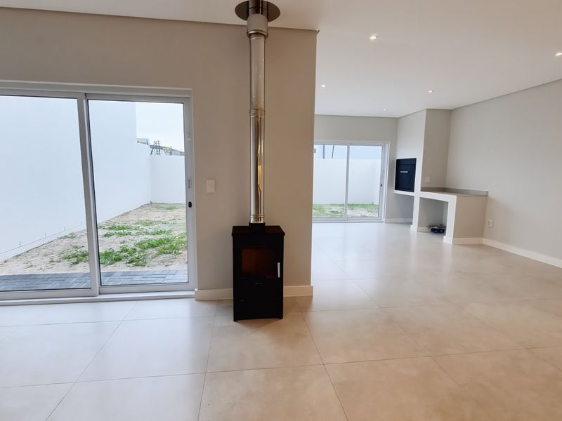 Spacious open-plan living area featuring large sliding doors, a modern freestanding fireplace, and a built-in braai, perfect for indoor-outdoor entertaining.