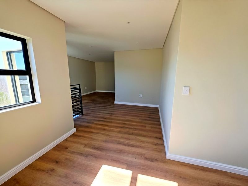 An empty, open-plan living area featuring modern laminate flooring, neutral walls, and a metal staircase railing, offering a clean and versatile space.