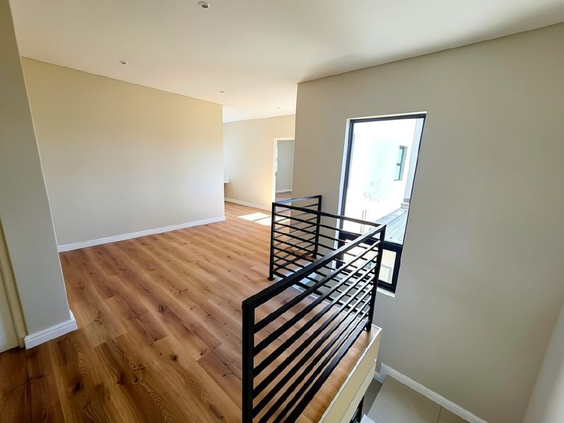 A bright and modern landing area featuring high-quality laminate flooring, a sleek black metal balustrade, and clean neutral wall finishes.