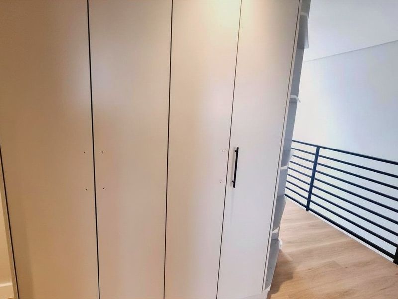 A bright hallway featuring modern built-in cabinetry and a sleek black metal balustrade overlooking the lower level.