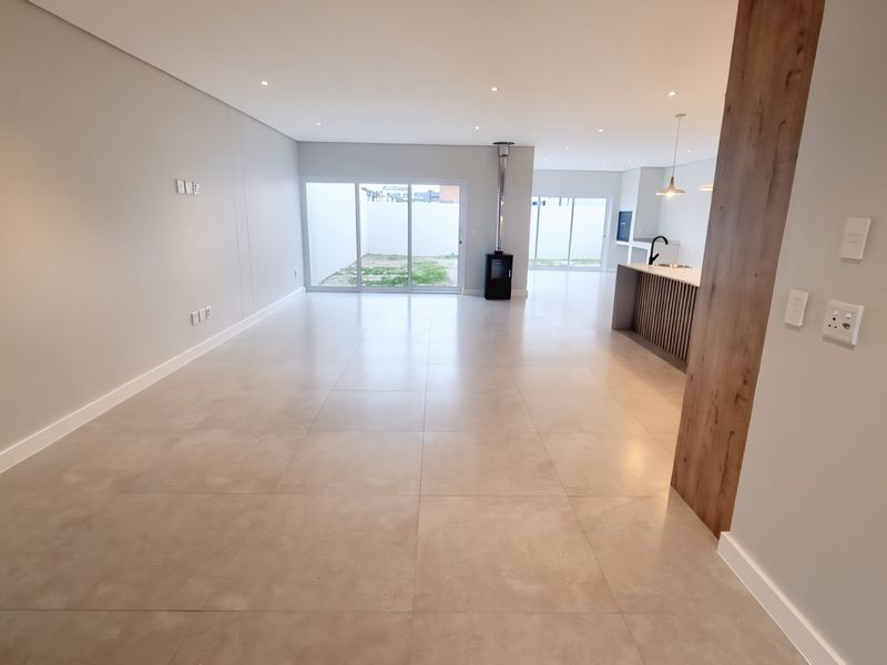 Spacious open-plan living and kitchen area featuring large format floor tiles, a modern fireplace, and seamless access to the rear outdoor space.