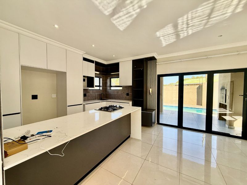 Modern kitchen featuring sleek built-in cabinetry, stone countertops, and a gas hob, with seamless access to the outdoor pool area through sliding glass doors.