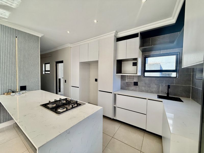 Modern kitchen featuring white cabinetry, stone countertops, a central island with a gas hob, and sleek black fixtures in a clean, contemporary space.