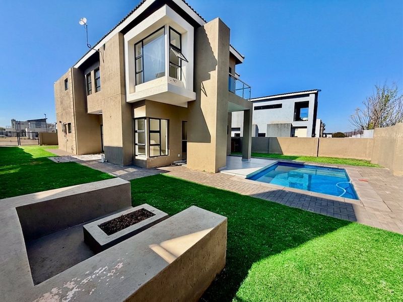 Rear exterior view of a modern double-story house featuring a swimming pool, paved patio area, and a built-in concrete fire pit.