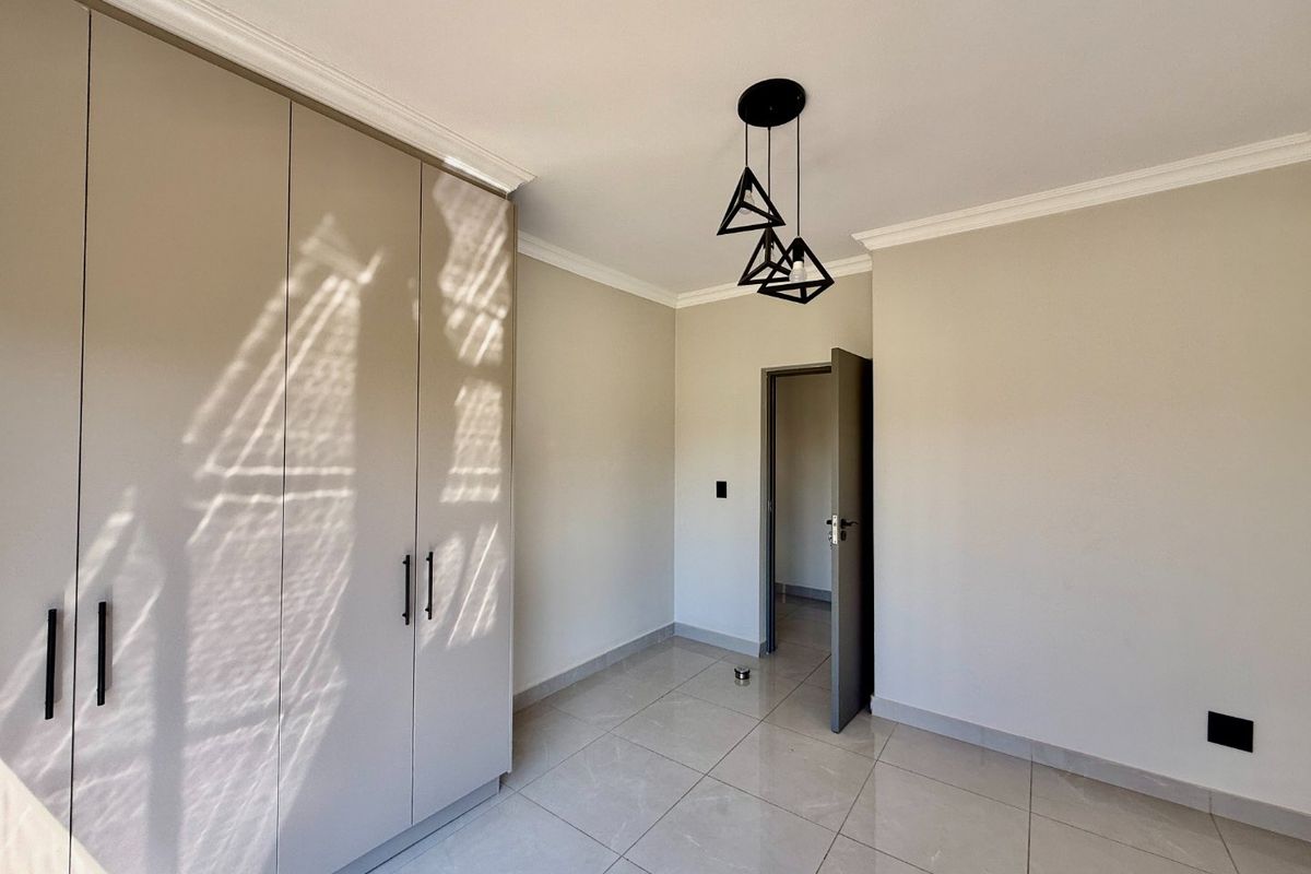 A bright, modern bedroom featuring neutral walls, large-format floor tiles, and ample built-in cupboard storage with contemporary finishes.