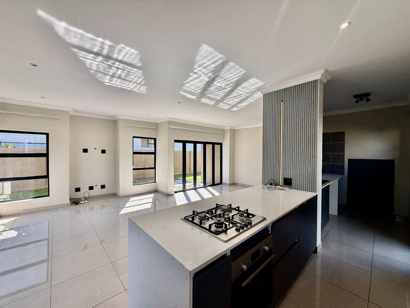 Modern open-plan living area featuring a sleek kitchen island with gas hob, stone countertops, and large aluminium stacker doors leading to the garden.