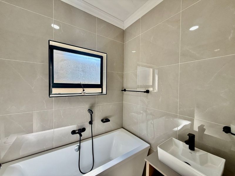 Modern bathroom featuring large format porcelain wall tiles, a sleek freestanding bathtub, vessel sink, and contemporary black matte fixtures.