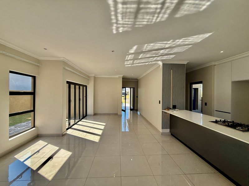 Spacious open-plan living and kitchen area featuring modern cabinetry, a stone island with gas hob, tiled floors, and large stacker doors leading outdoors.
