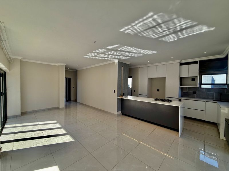 Spacious open-plan living and kitchen area featuring modern cabinetry, a central island with a gas hob, and polished tiled flooring throughout.
