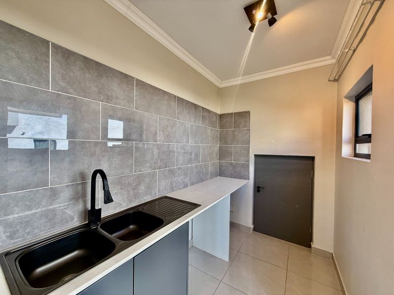 A clean and modern scullery featuring grey tiled splashbacks, a double sink with a black mixer tap, and ample countertop space.