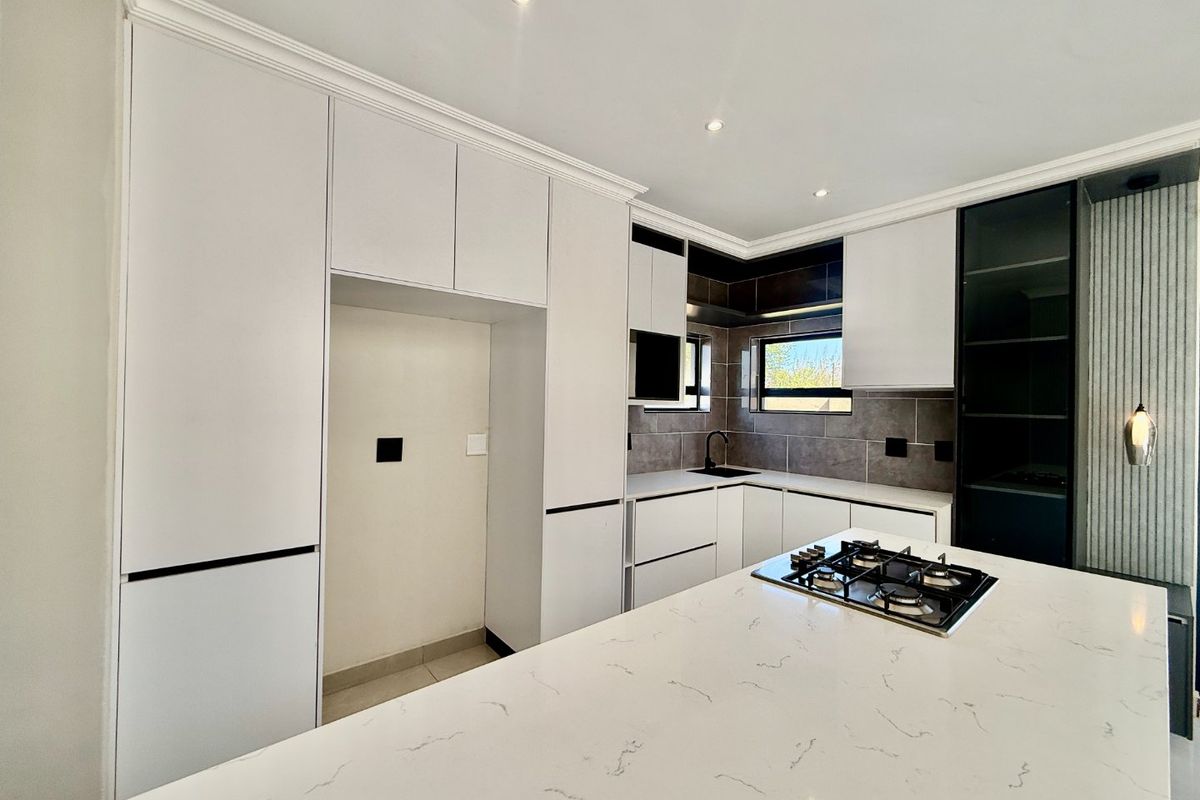 Modern kitchen featuring sleek white cabinetry, stone countertops, a central island with a gas hob, and contemporary tiled backsplash.