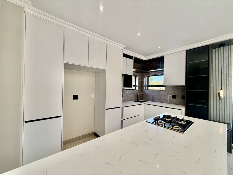 Modern kitchen featuring sleek white cabinetry, stone countertops, a central island with a gas hob, and contemporary tiled backsplash.