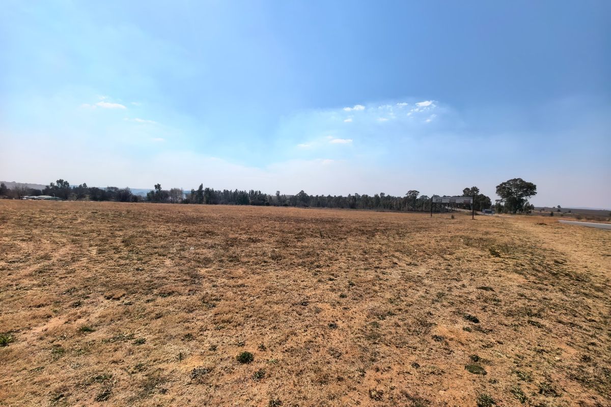 A wide-angle view of a large, flat, vacant residential plot of land with dry grass and clear horizon.