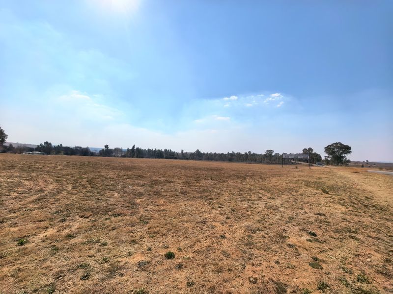 A wide-angle view of a large, flat, vacant residential plot of land with dry grass and open sky.