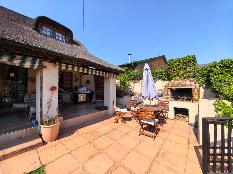 Covered patio area featuring a traditional thatched roof, tiled flooring, and a built-in brick braai, ideal for outdoor entertaining.