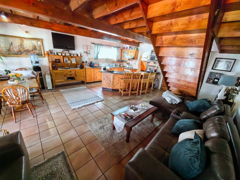 Spacious open-plan living and kitchen area featuring exposed timber ceiling beams, a wooden staircase, and tiled flooring throughout.