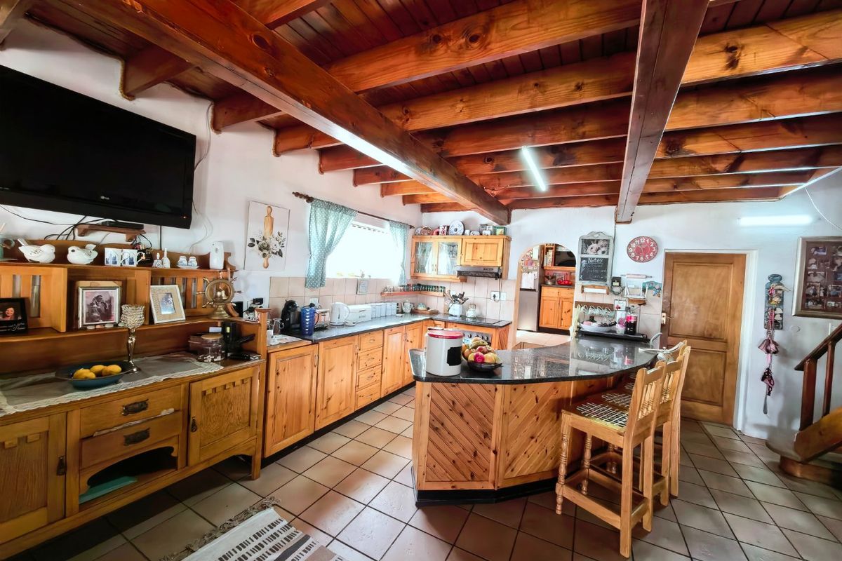 A rustic kitchen featuring exposed timber ceiling beams, extensive wooden cabinetry, granite countertops, and a breakfast bar, with tiled flooring throughout.