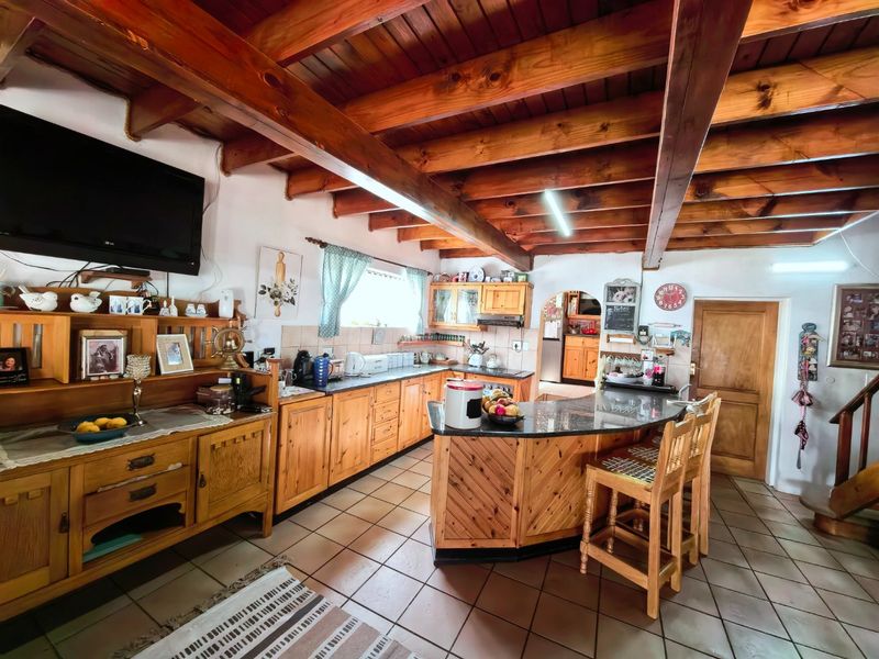 A rustic kitchen featuring exposed timber ceiling beams, extensive wooden cabinetry, granite countertops, and a breakfast bar, with tiled flooring throughout.