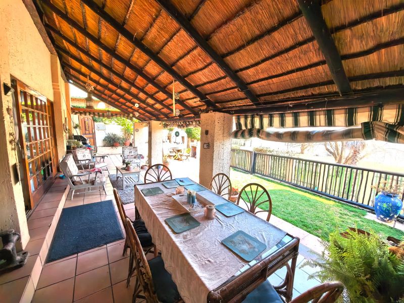Spacious covered patio featuring a traditional thatched roof, tiled flooring, and a metal railing overlooking the garden area.