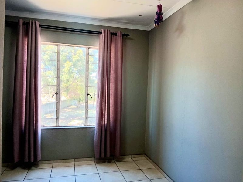 A simple, empty bedroom featuring tiled flooring, a window with security bars, and neutral wall finishes.