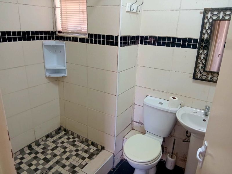 A compact bathroom featuring a shower cubicle, pedestal basin, and toilet, finished with dated wall and floor tiling.