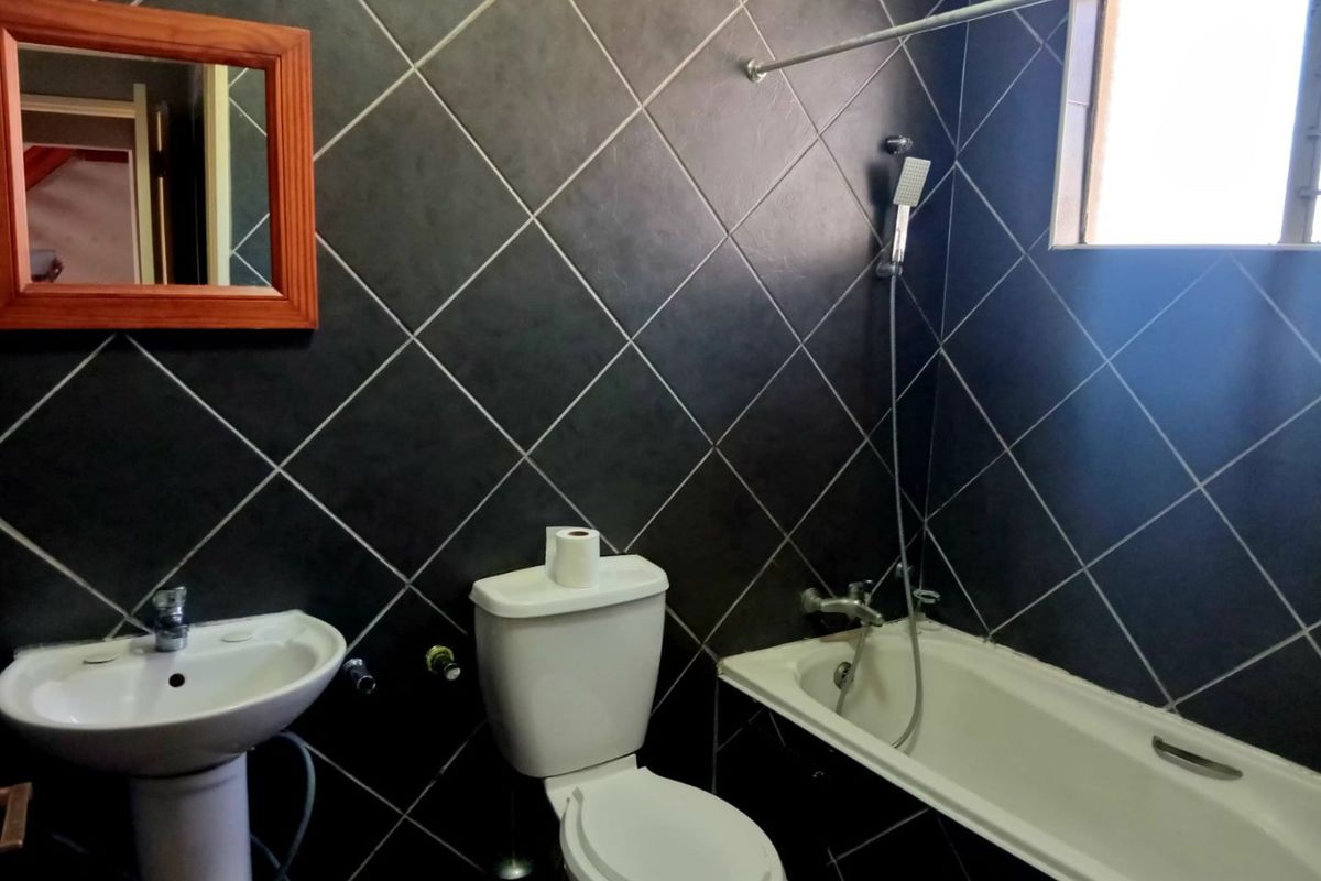 A bathroom featuring dark diamond-patterned wall tiles, a pedestal basin, a toilet, and a bathtub with a handheld shower attachment.