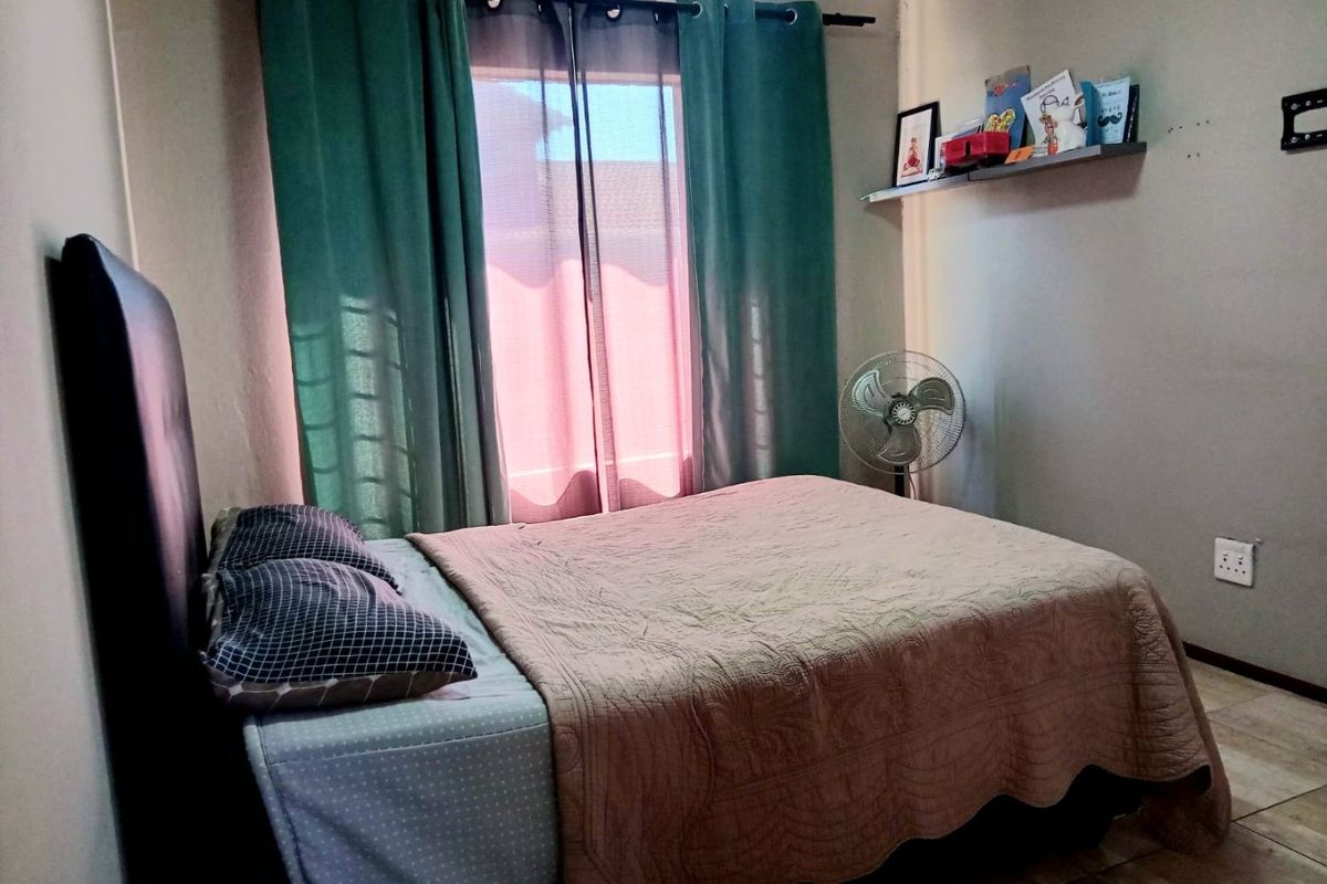 A functional bedroom featuring tiled flooring, a wall-mounted shelf, and a window with curtain fixtures.