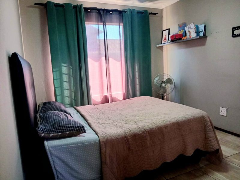 A functional bedroom featuring tiled flooring, a wall-mounted shelf, and a window with curtain fixtures.
