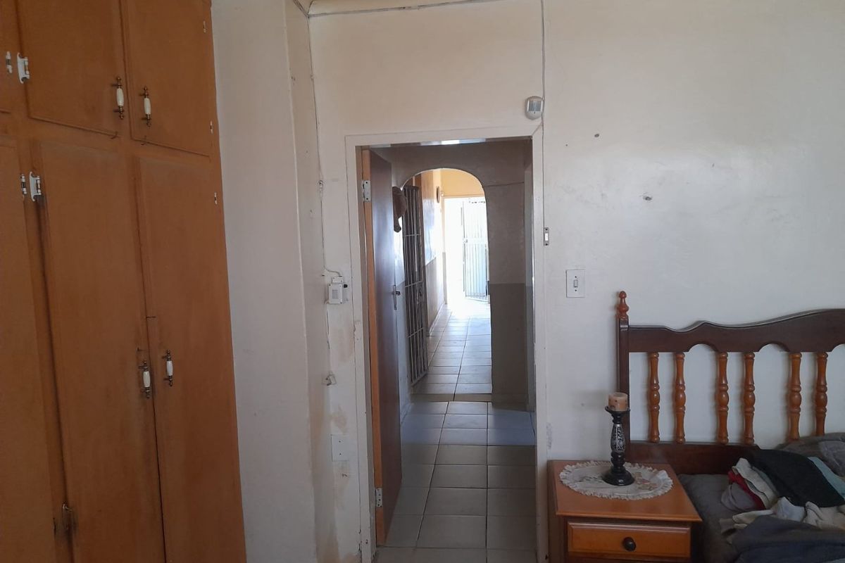 A bedroom featuring built-in wooden cupboards and an arched doorway leading to a tiled hallway, showing signs of wear on the wall finishes.