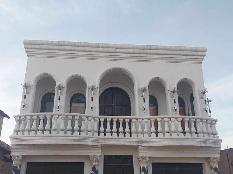 Front elevation of an apartment building featuring a prominent balcony with a stone balustrade, arched architectural details, and decorative exterior lighting.