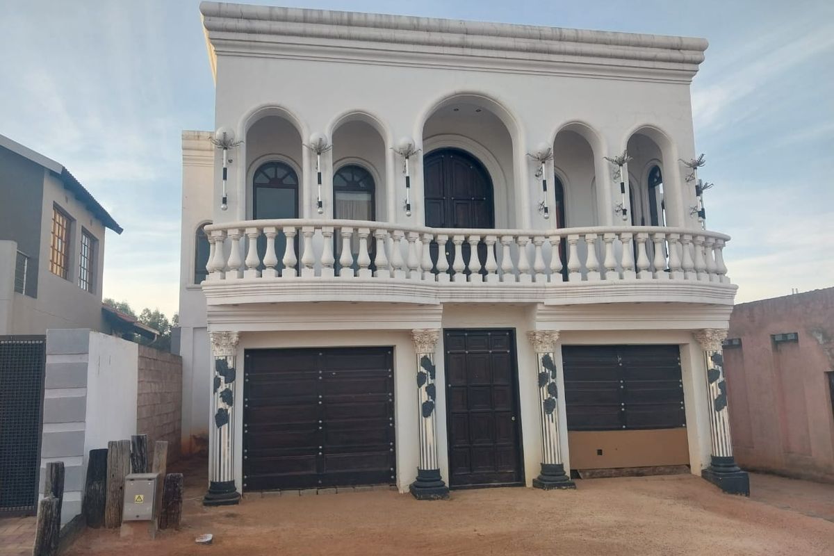 Front elevation of a two-story property featuring a balcony with balustrades, arched architectural details, decorative columns, and a double garage.