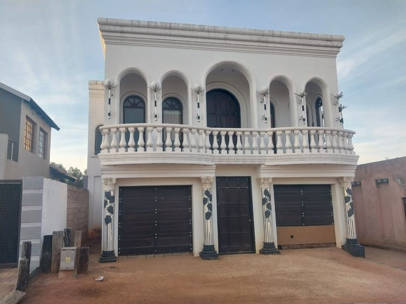 Front elevation of a two-story property featuring a balcony with balustrades, arched architectural details, decorative columns, and a double garage.