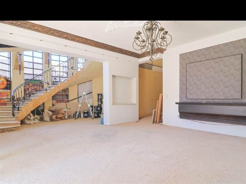 Spacious living area featuring a grand staircase with wrought iron railing, decorative ceiling details, and a built-in feature wall, currently undergoing renovation.