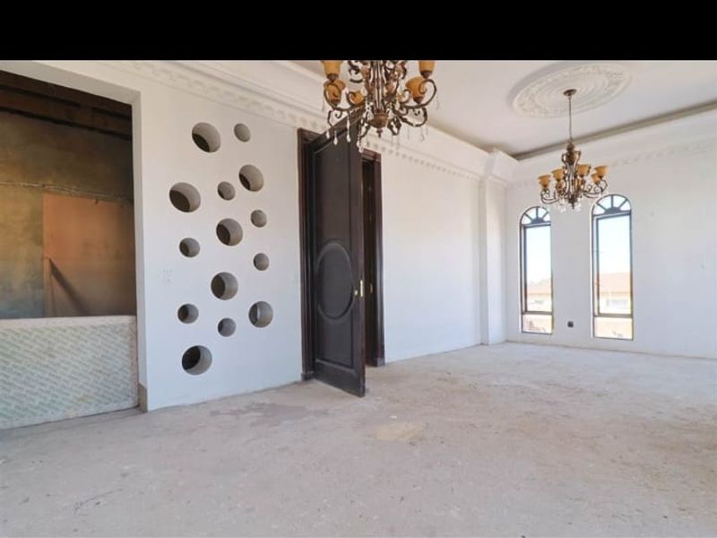 Spacious living area featuring ornate crown molding, decorative ceiling roses, arched windows, and a unique circular cutout feature wall, currently awaiting final flooring installation.