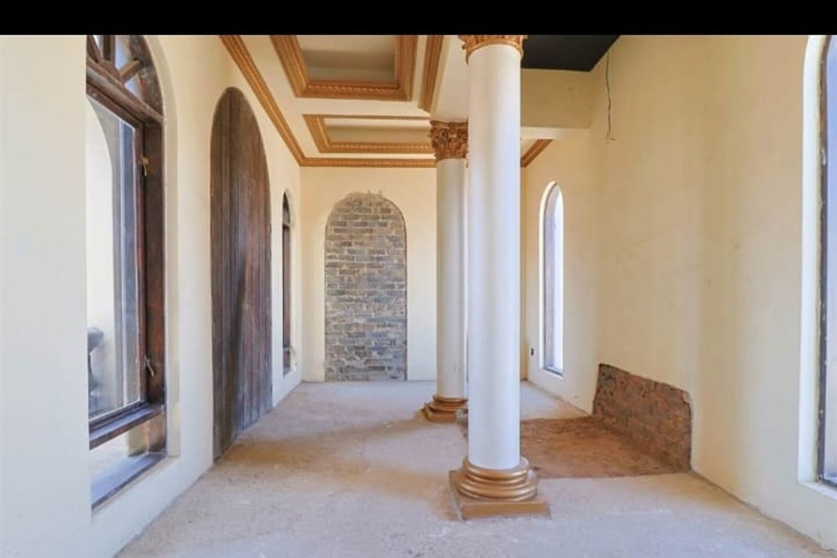 An empty living area featuring decorative columns, arched windows, and a coffered ceiling, currently requiring floor and wall finishing to complete the space.