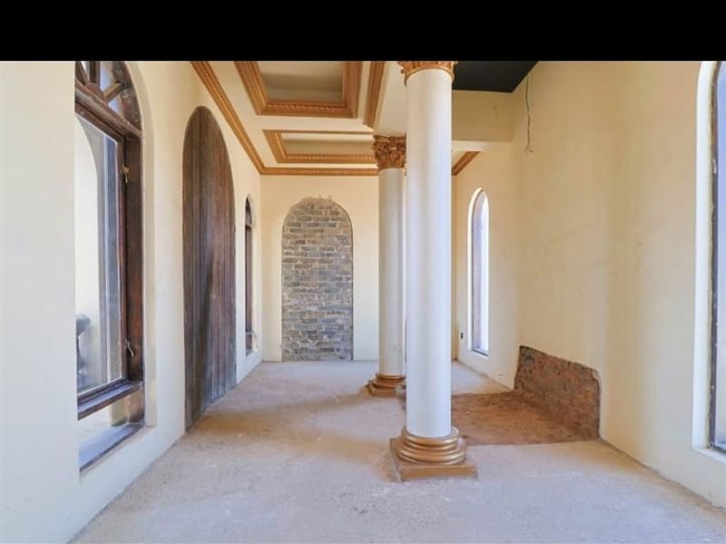 An empty living area featuring decorative columns, arched windows, and a coffered ceiling, currently requiring floor and wall finishing to complete the space.