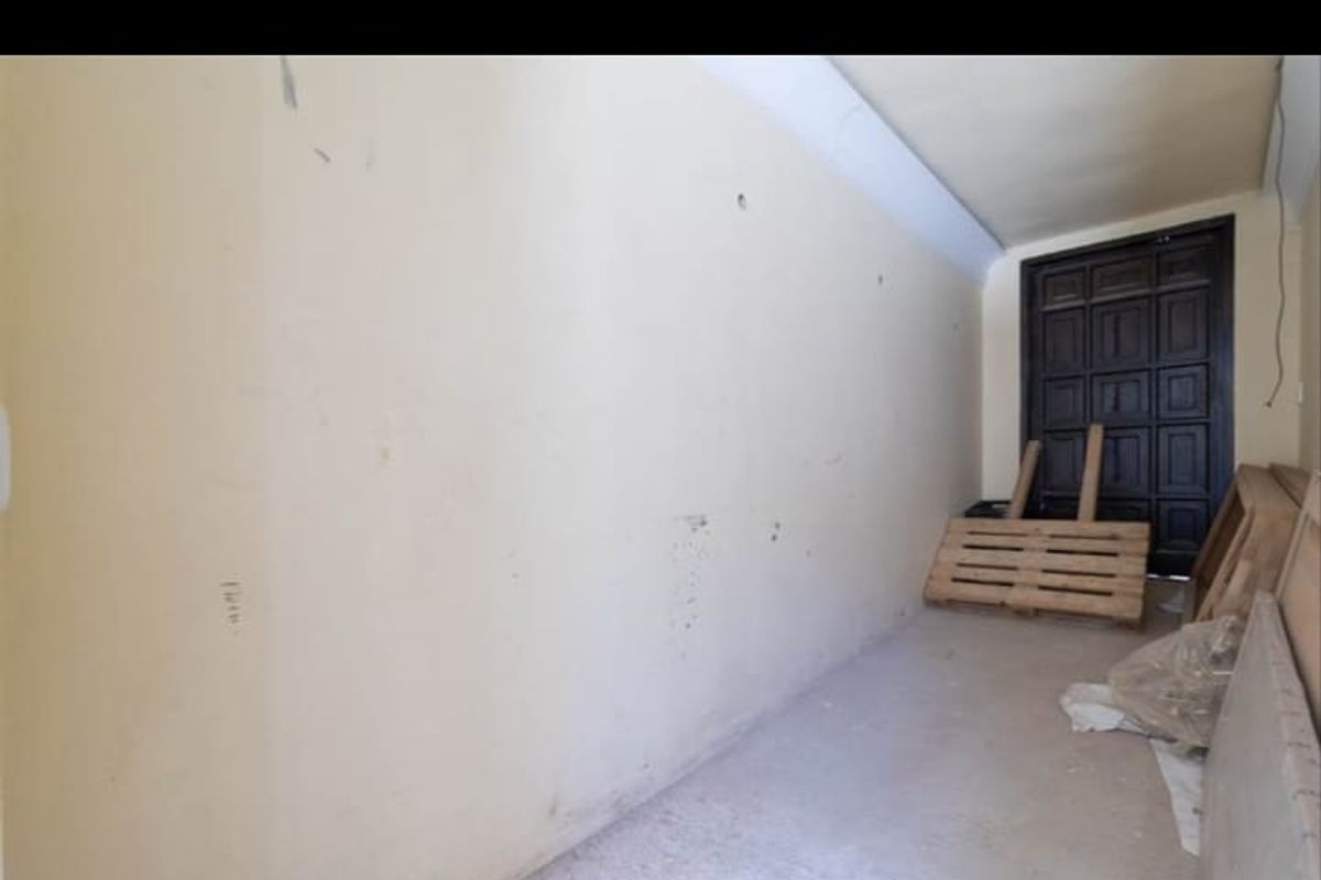 An empty utility or storage space featuring a dark panelled door and unfinished wall and floor surfaces.