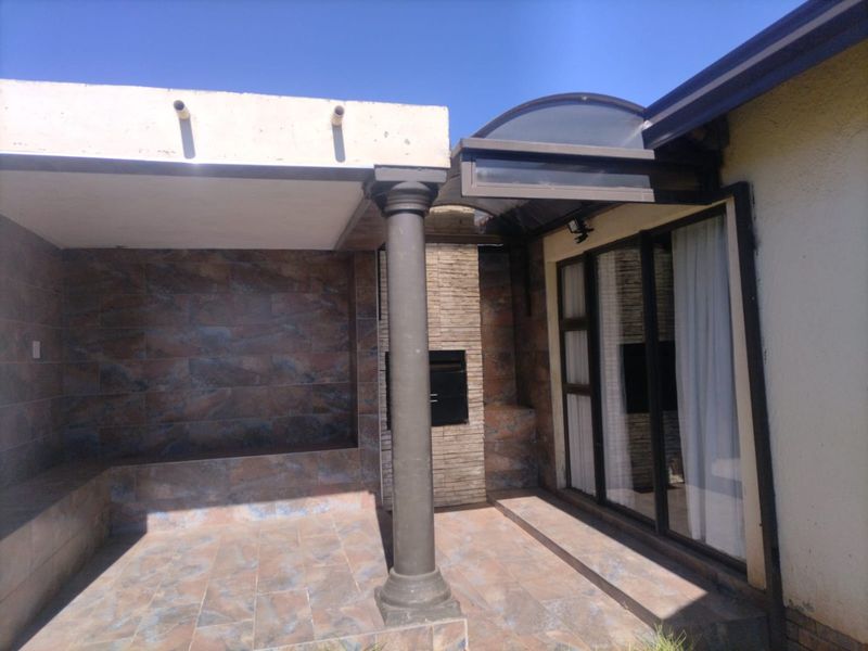 Covered patio area featuring a built-in braai, stone-clad feature wall, tiled flooring, and sliding glass door access to the interior.