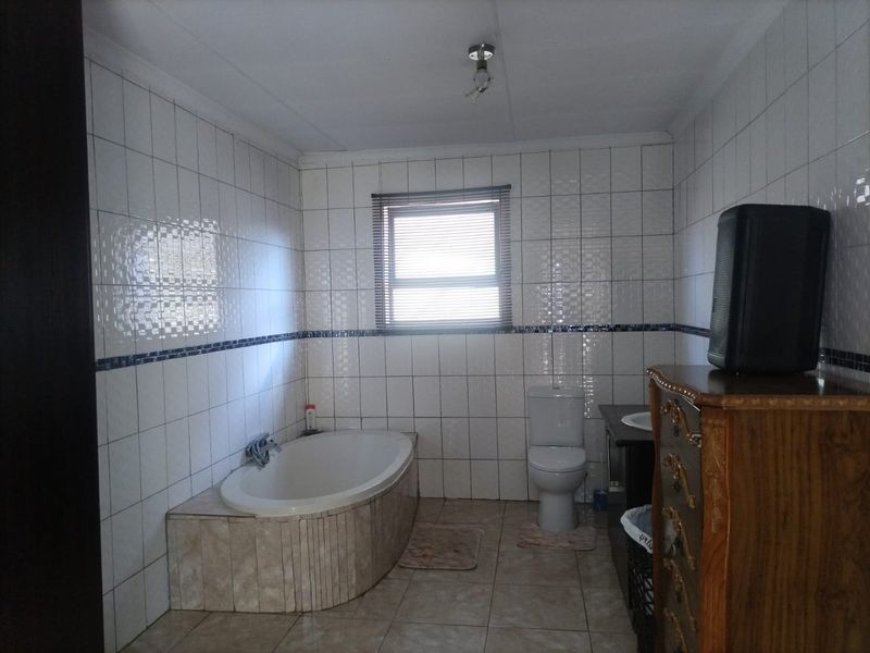 A functional bathroom featuring a built-in bathtub, toilet, and vanity cabinet with full-height wall tiling and tiled flooring.