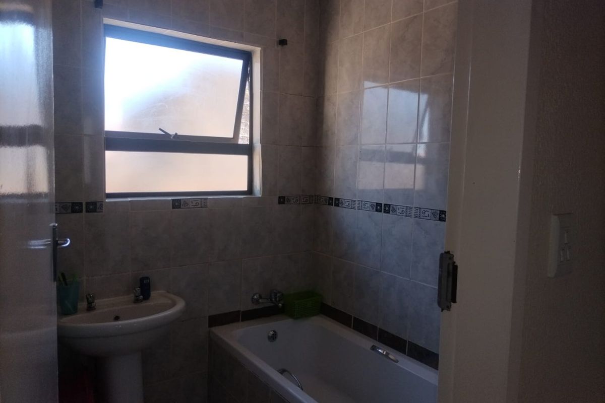 A functional bathroom featuring a pedestal basin, bathtub, and tiled walls with a top-hung window for natural light.