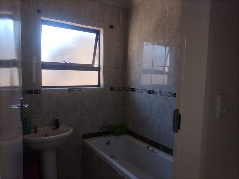 A functional bathroom featuring a pedestal basin, bathtub, and tiled walls with a top-hung window for natural light.