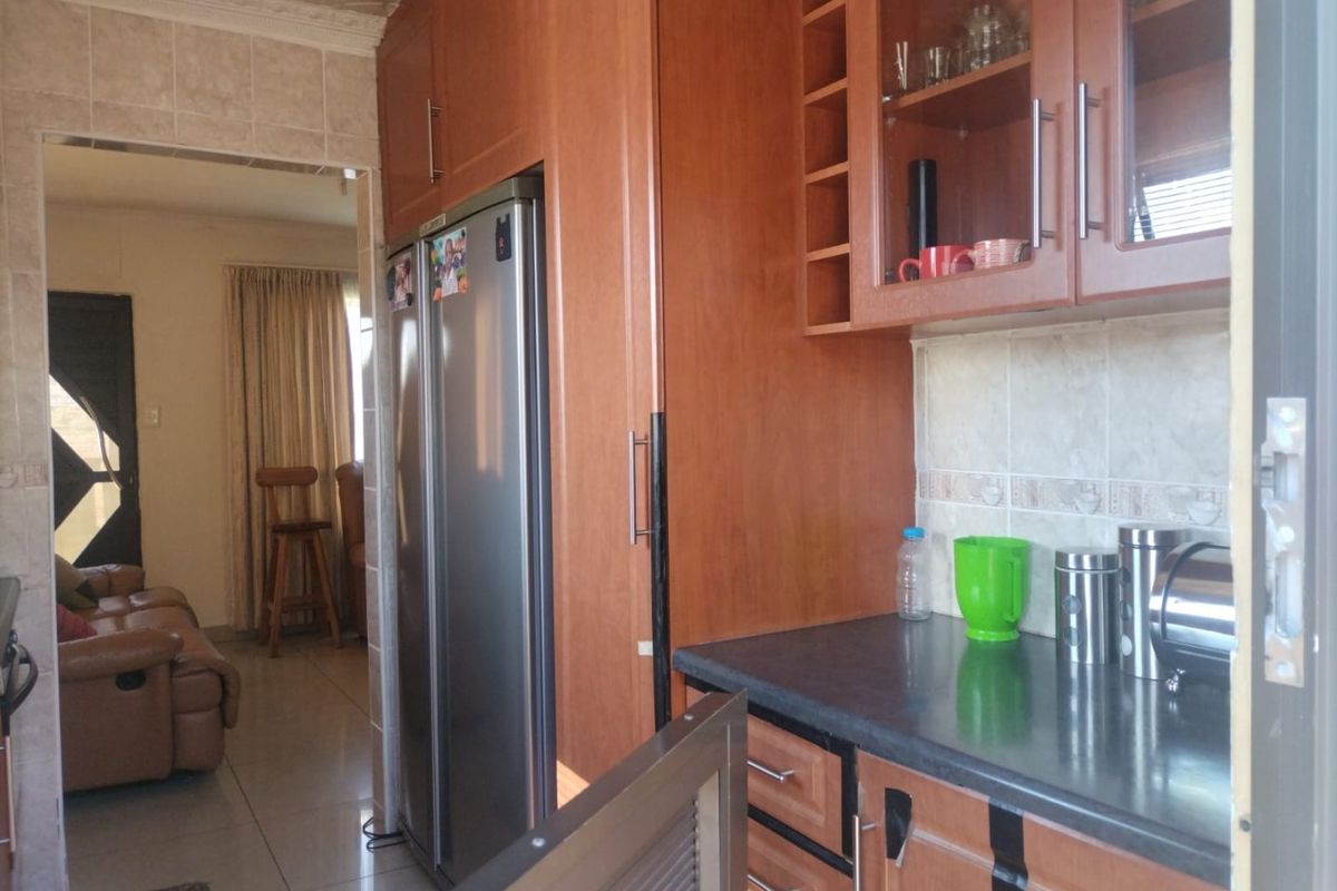 A functional kitchen featuring wood-finish cabinetry, dark laminate countertops, and a tiled backsplash, with an open transition into the adjacent living area.