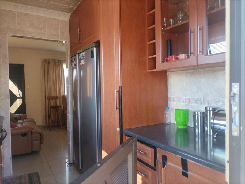 A functional kitchen featuring wood-finish cabinetry, dark laminate countertops, and a tiled backsplash, with an open transition into the adjacent living area.