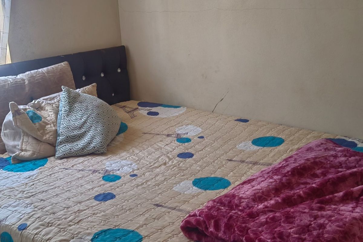A bedroom featuring a window and plain wall finishes, showing signs of wear and tear on the wall surface.